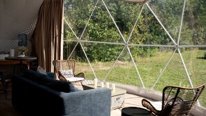 A tented accommodation with a view of a grassy area and trees, furnished with a sofa, chairs, and a table. - Unique Off-Grid Dome Escape with Hot Tub & Forest Views in Ontario, Canada (Marmora)