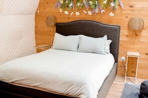 Una cama con cabecera acolchada, dos mesitas de noche y una lámpara de pared.