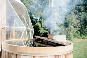 Un jacuzzi con tapa transparente, vapor ascendiendo y una estructura de madera.