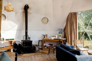 Un intérieur chaleureux avec un poêle à bois, un coin repas et une grande fenêtre agrémentée de rideaux.