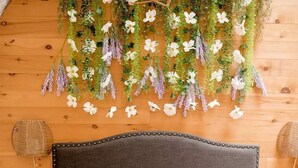 A bed with white bedding, a dark headboard, and a wooden wall with hanging floral decorations. - Unique Off-Grid Dome Escape with Hot Tub & Forest Views in Ontario, Canada (Marmora)