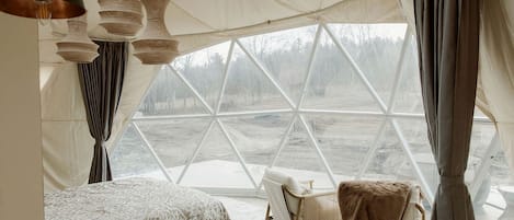 A tent-style room with a bed, two chairs, and hanging light fixtures.
