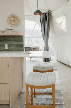 Una habitación con tienda de campaña, un banco de madera, una mesa blanca y una lámpara colgante.
