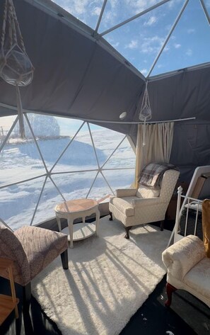 A cozy interior with a large window, a cushioned chair, a small table, and a hanging light fixture. - Tranquil Dome on the Calm Prairies of Alberta, Canada, near Medicine Hat and Redcliff (Redcliff)