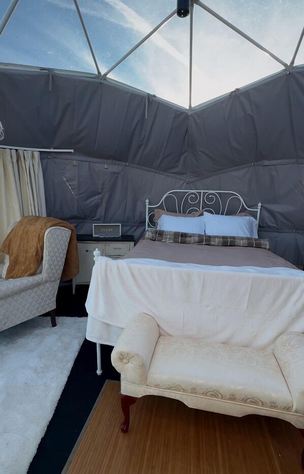 A tented room with a bed, bedside table, lamp, and a chair.
