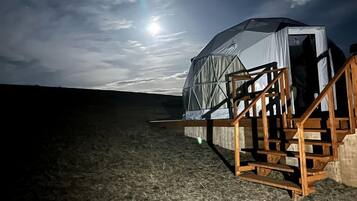 Una tienda de campaña abovedada con una escalera que lleva a la entrada, ubicada en un campo cubierto de hierba bajo un cielo nocturno con una luna visible.