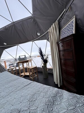 A tented room with a bed, wooden furniture, a dresser, and a view of the water.