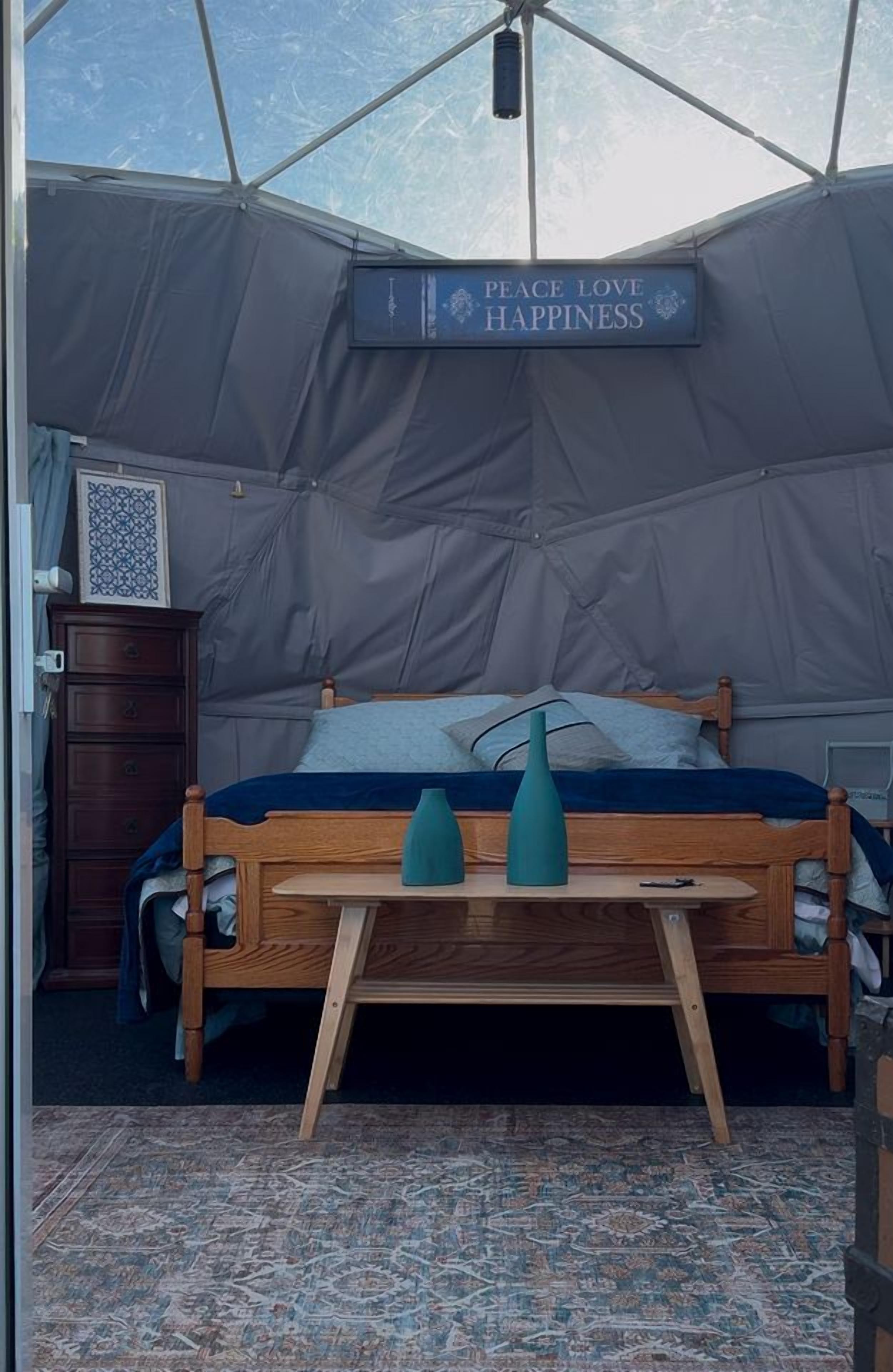 Une pièce aménagée avec une tente, un lit, une commode et une pancarte sur laquelle on peut lire : « Paix, amour, bonheur ».