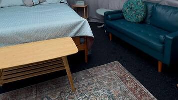 A tented room with a bed, a bench, a sofa, a small table, and a rug.