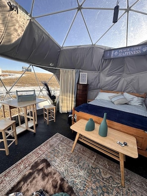A tented accommodation with a bed, a small table, a chair, and a rug.