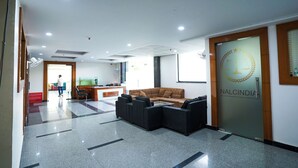 Un vestíbulo moderno con un mostrador de recepción, un sofá marrón y una puerta de cristal con el nombre 'NALCINDIA'.