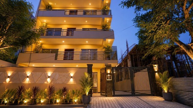 Un edificio de varios pisos con balcones, entrada protegida por un portón y plantas en macetas.