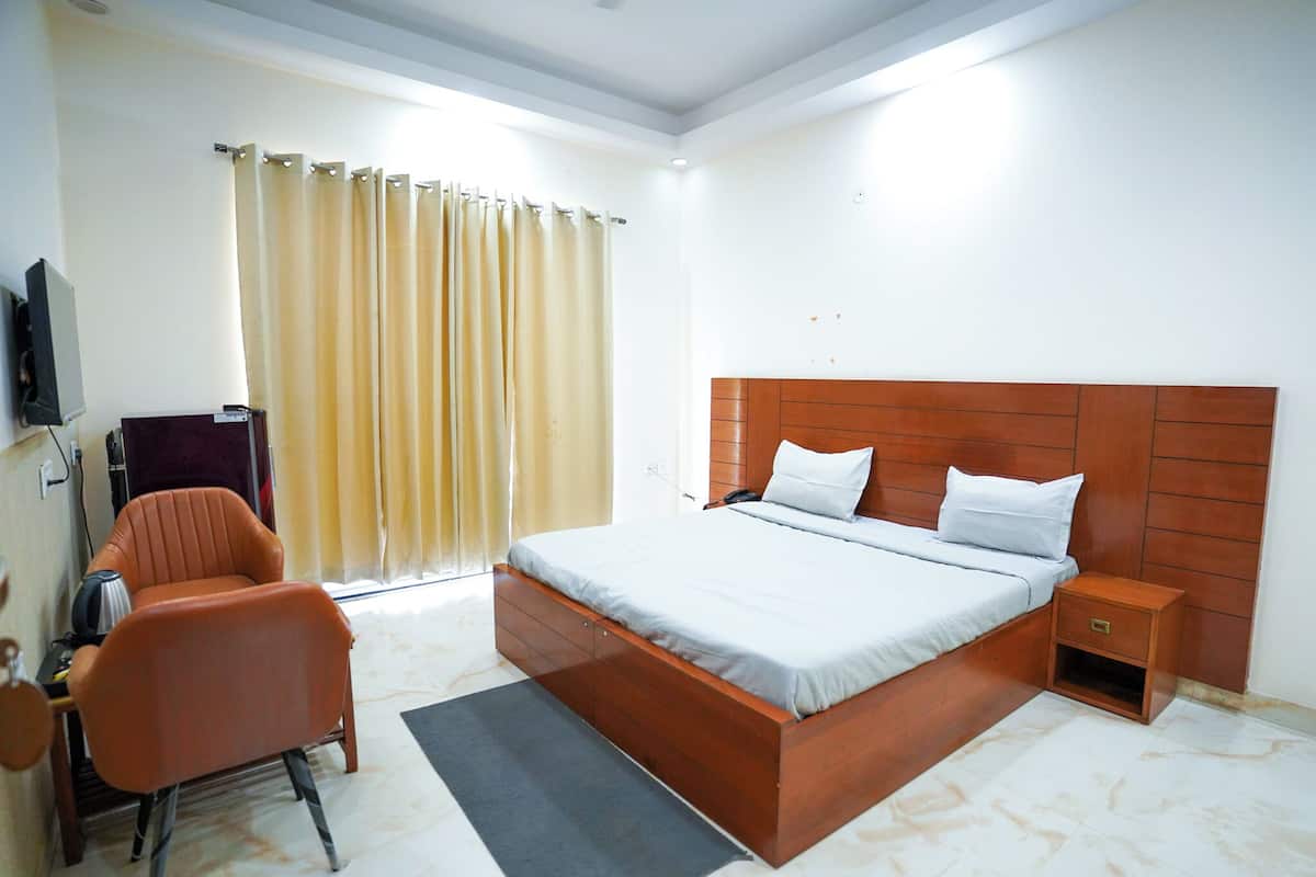 A hotel room with a bed, a chair, a nightstand, a television, and a window with curtains.