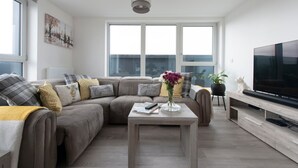 A modern living room with a sectional sofa, a flat-screen TV, and a large window. - Stylish Penthouse- Guests Favourite Just Amazing (London)