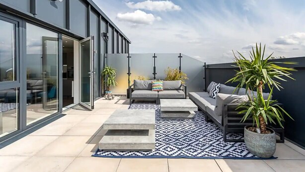 A modern outdoor living area with a sofa, coffee table, and potted plants. - Stylish Penthouse- Guests Favourite Just Amazing (London)