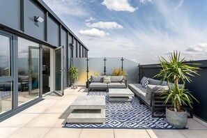 A modern outdoor living area with a sofa, coffee table, and potted plants. - Stylish Penthouse- Guests Favourite Just Amazing (London)