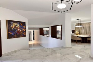 Un couloir doté d’un sol en marbre, d’un tableau accroché au mur et d’un coin repas avec une table et des chaises.