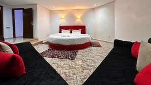 A bedroom with a bed, two wall-mounted lights, a red headboard, and a patterned rug. - Maison Ciel (Tanger)