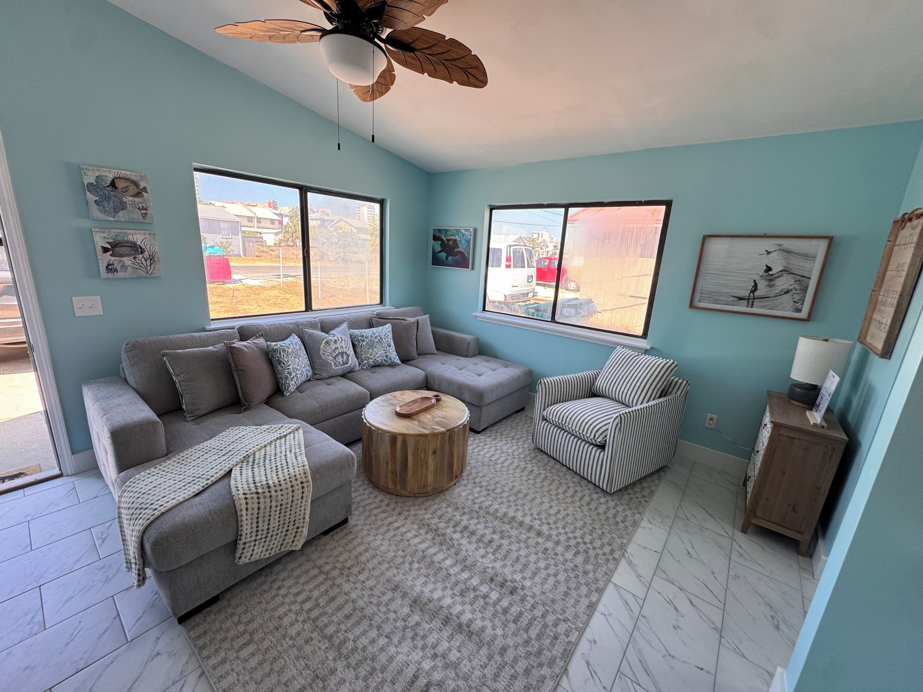 A living room with a grey sofa, a striped armchair, a round wooden coffee table, and a ceiling fan.