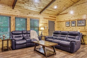 A cozy room with two leather sofas, a wooden coffee table, and a large window with blinds. - Secluded 3bdrm/2bth cabin with hiking trail & bonfire pit, Peaceful Path (Townsend)