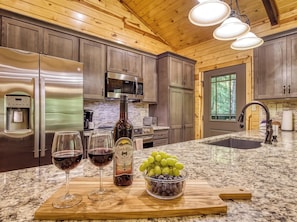 A kitchen with stainless steel appliances, a wine bottle, and glasses on a granite countertop. - Secluded 3bdrm/2bth cabin with hiking trail & bonfire pit, Peaceful Path (Townsend)