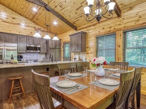 A wooden cabin interior with a kitchen, dining area, and large windows. - Secluded 3bdrm/2bth cabin with hiking trail & bonfire pit, Peaceful Path (Townsend)