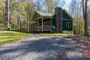 Eine Lodge mit Veranda, Steinofen und Kiesweg, umgeben von Bäumen.