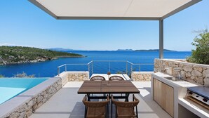 Eine Terrasse mit Tisch, Stühlen, einer Steinsäule, einem Waschbecken und Blick aufs Meer.