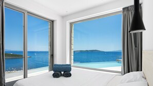 Ein Hotelzimmer mit Bett, einer kleinen Sitzecke und einem großen Fenster mit Blick auf das Meer und das entfernte Land.