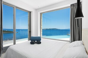 Ein Hotelzimmer mit Bett, einer kleinen Sitzecke und einem großen Fenster mit Blick auf das Meer und das entfernte Land.