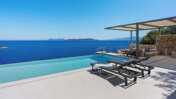 Ein Pool ohne Ende mit Blick aufs Meer, Sitzgelegenheiten im Freien und eine Steinsäule.
