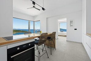 Eine moderne Küche mit einer großen Kochinsel, zwei Barhocker und Blick aufs Meer.