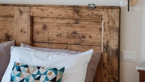 Una cama con cabecera de madera, almohada con estampado geométrico y una lámpara fijada a la pared.