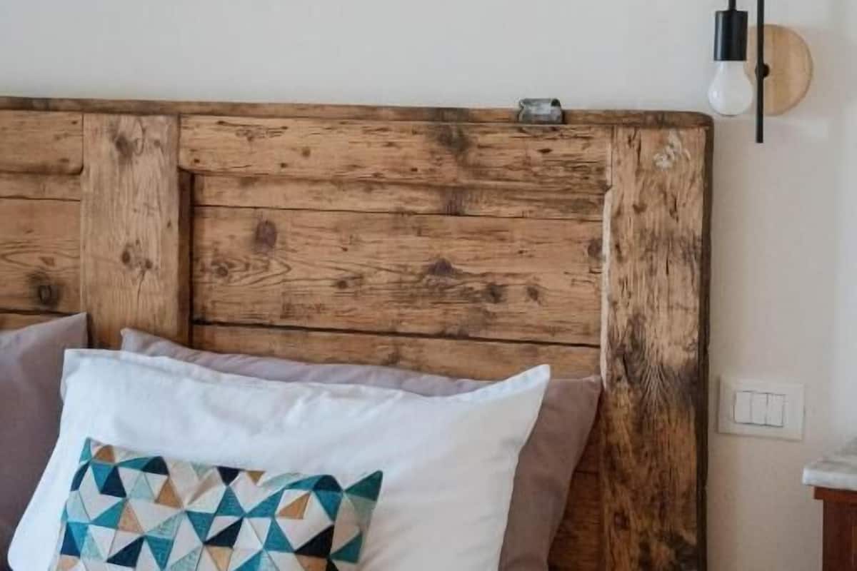 A bed with a wooden headboard, a geometric-patterned pillow, and a wall-mounted light fixture.