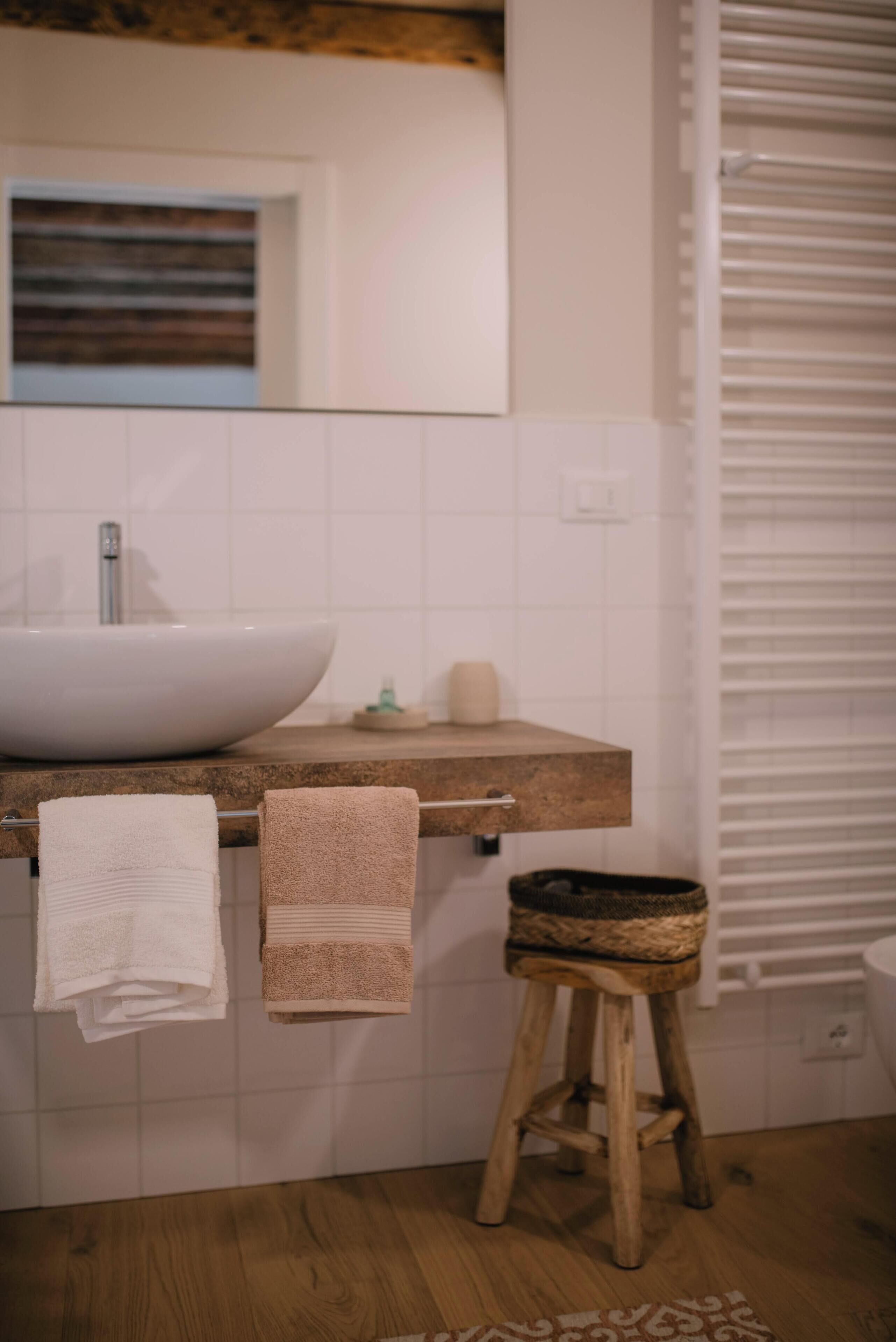 Une salle de bain avec un lavabo blanc, un tabouret en bois et un porte-serviettes.