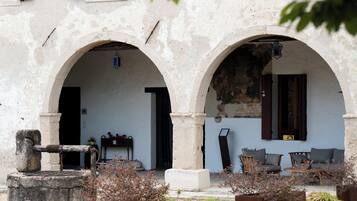 Un bâtiment doté de deux portes en arc de cercle, d’un mur en pierre et d’un espace aménagé avec du mobilier d’extérieur.