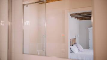 Ein Zimmer mit Duschkabine aus Glas, einem Bett mit weißer Bettwäsche und einem Holzbalken an der Decke.