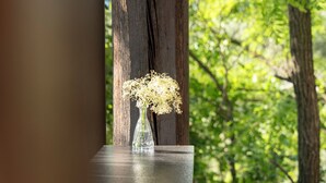 Una mesa de madera con un jarrón de vidrio transparente que contiene flores blancas, ubicada debajo de una viga de madera.