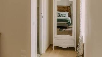 A narrow hallway with a white wardrobe, a door leading to a bedroom, and a wooden floor.