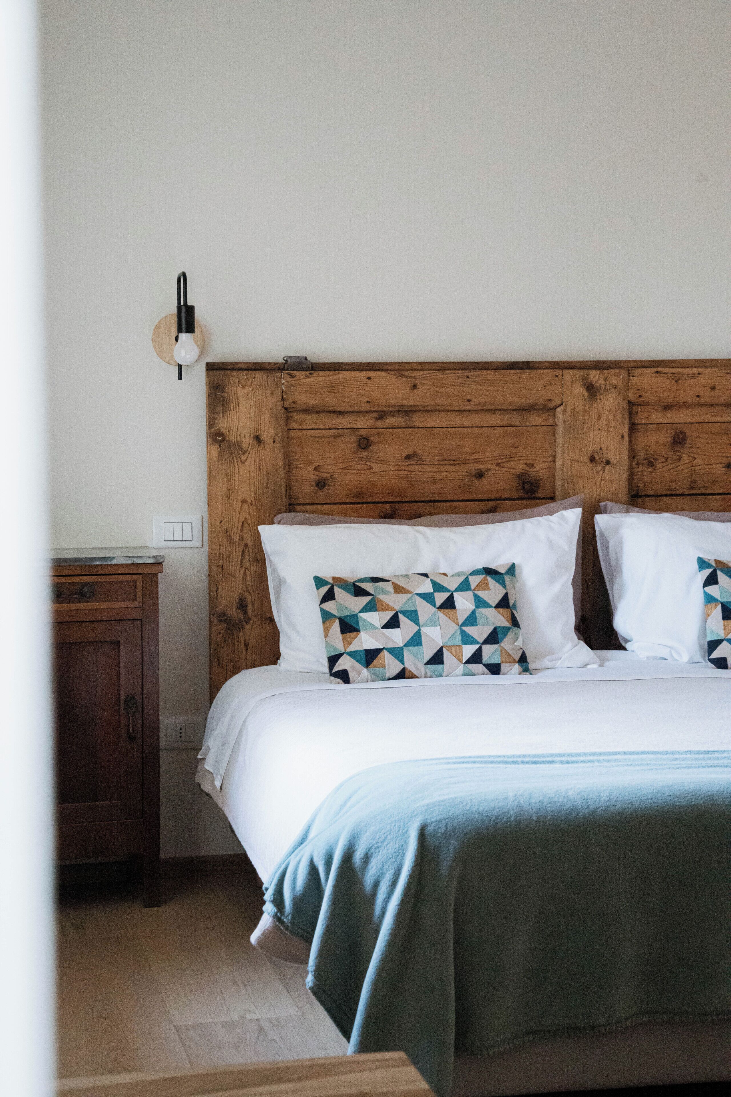 A bed with a wooden headboard, white bedding, and patterned pillows.