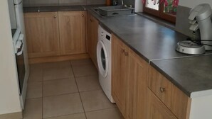 A kitchen with wooden cabinets, a washing machine, a countertop, and a small window.