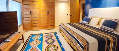 A bedroom with a large bed, a wooden wardrobe, a television, and a patterned rug.