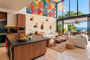 A modern living space with a kitchen, dining area, and a large window overlooking a scenic view. - Unique Designer Gem: Private Pool, Elevator, Views (Puerto Vallarta)