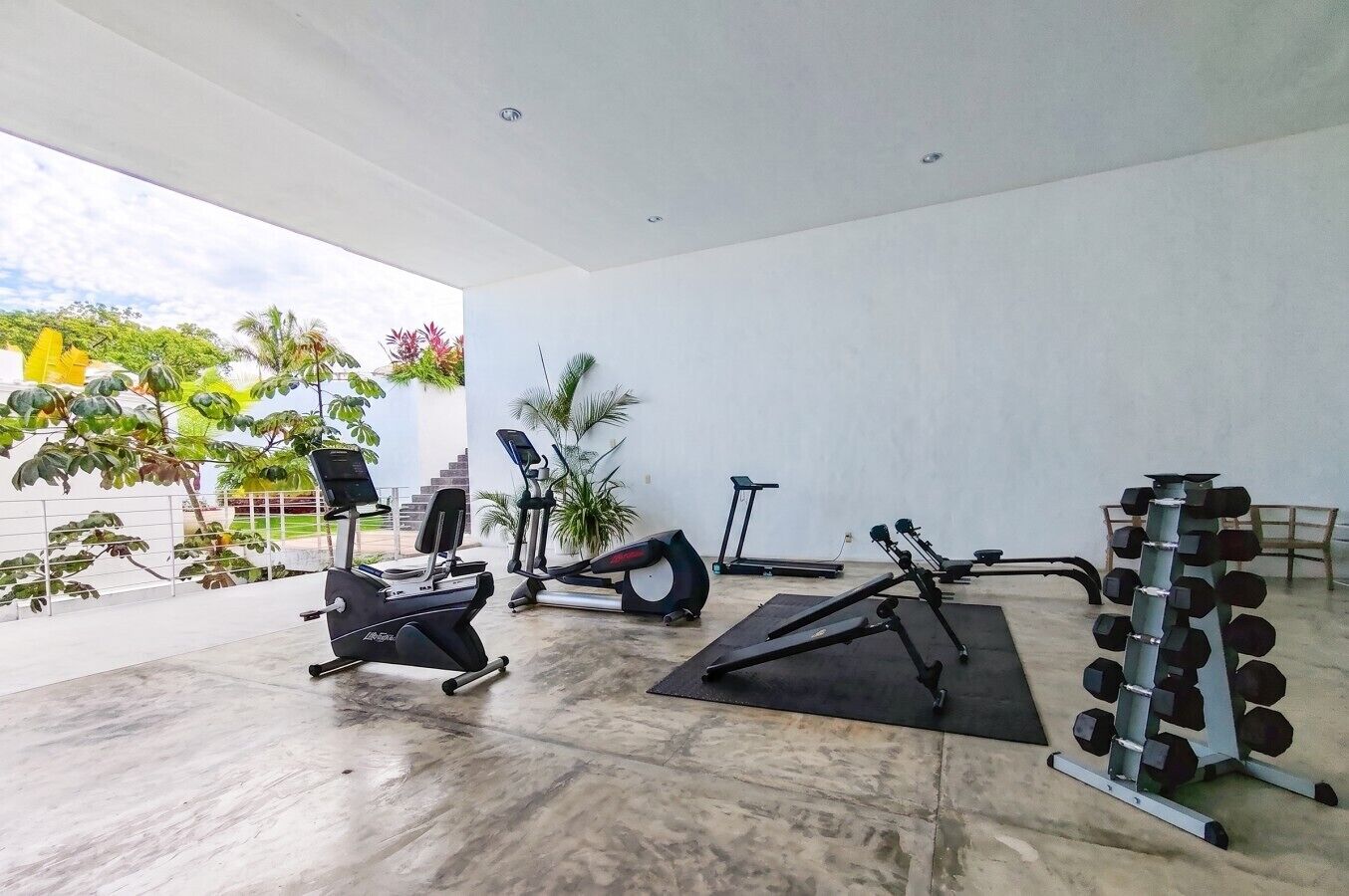 Academia com máquinas de cardio, um banco de musculação e uma barra com halteres.