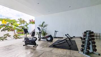 Academia com máquinas de cardio, um banco de musculação e uma barra com halteres.
