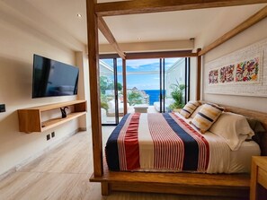 Quarto com uma cama grande, televisão na parede e varanda com vista para o mar.