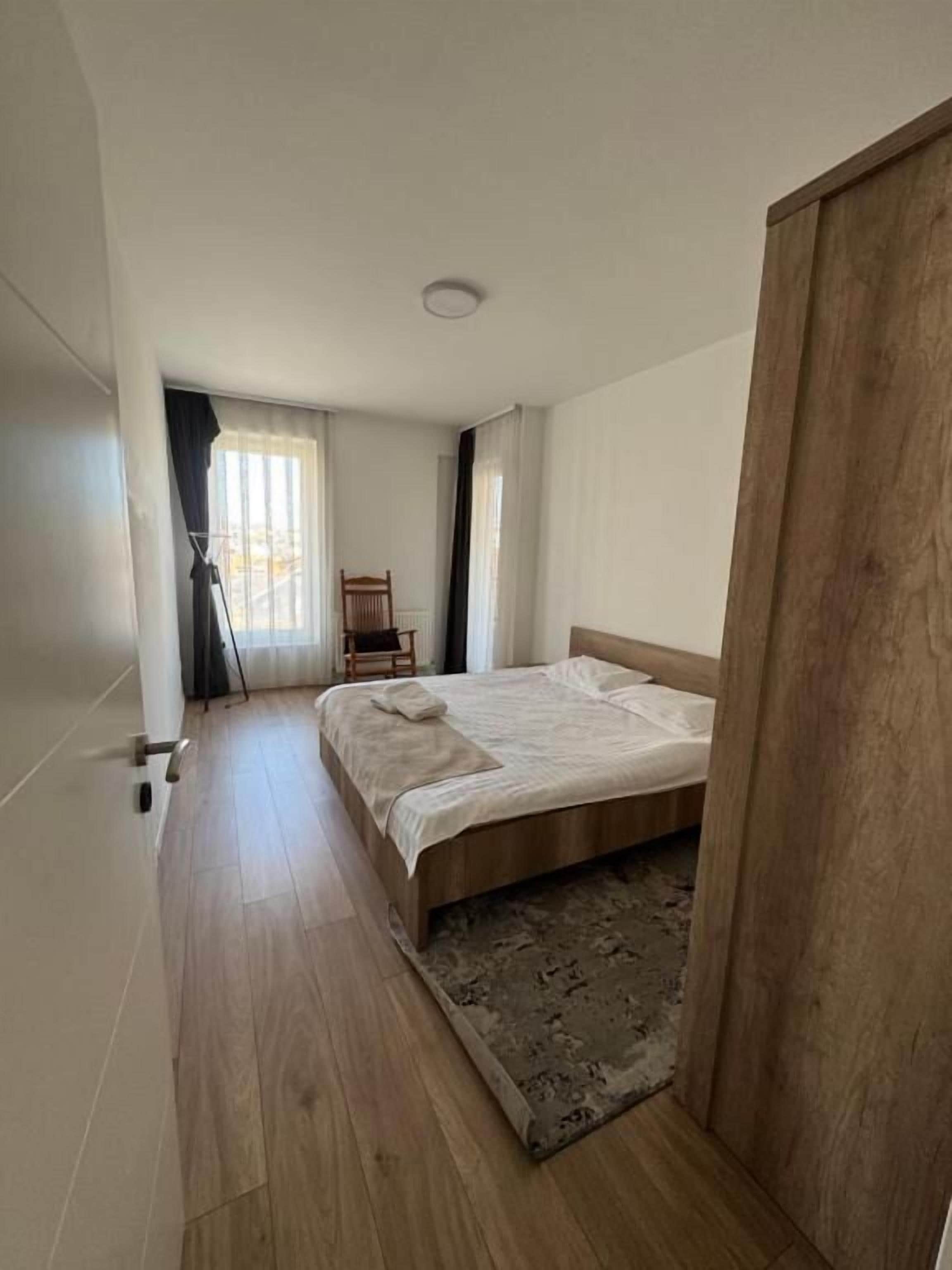 A bedroom with a wooden bed, a chair, a floor lamp, and a window with curtains.