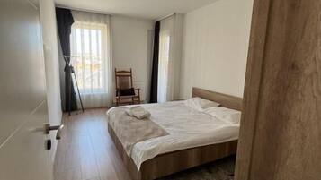 A bedroom with a wooden bed, a chair, a floor lamp, and a window with curtains.