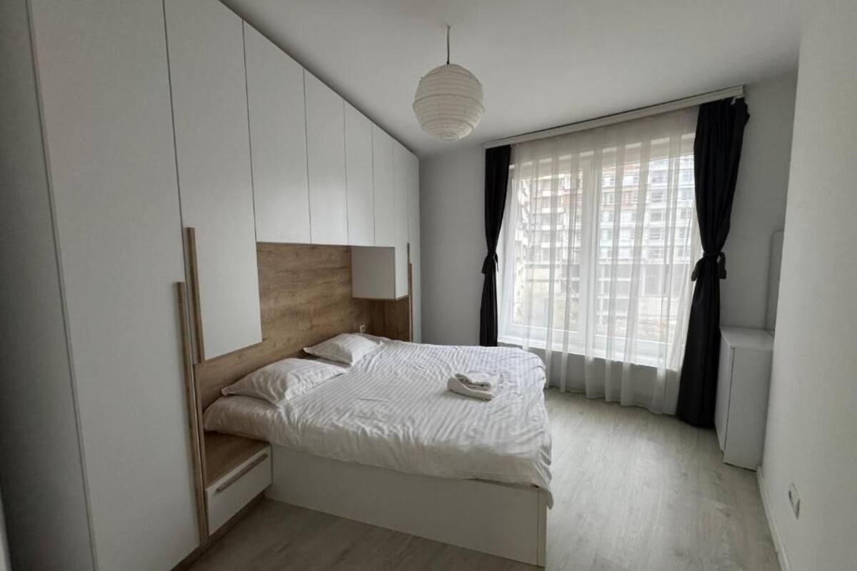 A bedroom with a bed, a wardrobe, a bedside table, and a window with curtains.