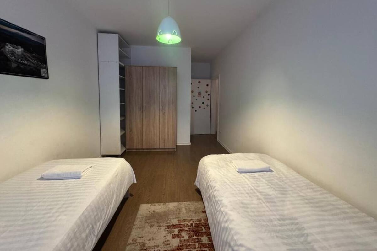 A bedroom with two beds, a wooden wardrobe, a white closet, and a hallway leading to a bathroom.